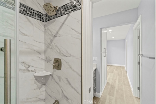 bathroom with baseboards, vanity, a marble finish shower, and wood finished floors