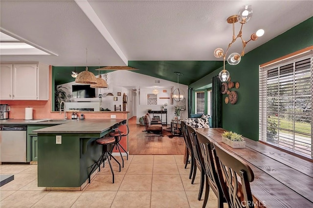 kitchen featuring light tile patterned floors, a kitchen bar, hanging light fixtures, stainless steel dishwasher, and white cabinets