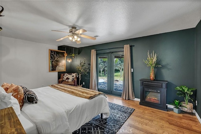 bedroom with ceiling fan, access to exterior, light hardwood / wood-style floors, a textured ceiling, and french doors