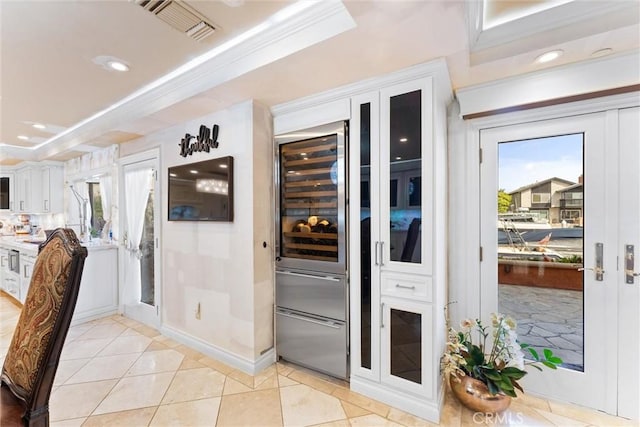 doorway to outside with light tile patterned floors, a tray ceiling, beverage cooler, and crown molding