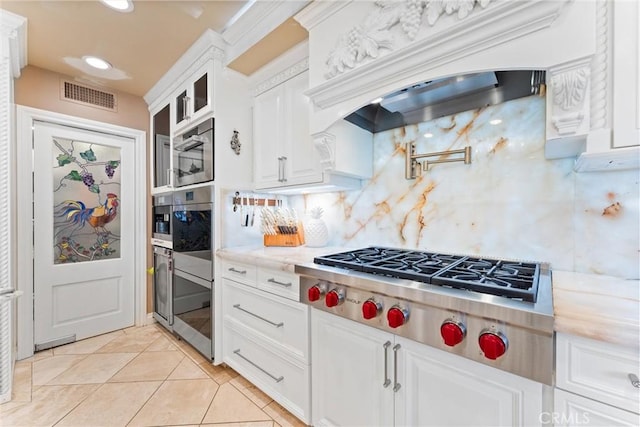 kitchen with backsplash, light tile patterned floors, light stone counters, white cabinetry, and stainless steel appliances