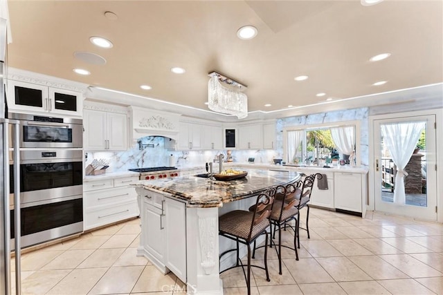 kitchen with white cabinets, backsplash, light stone countertops, and a kitchen island with sink