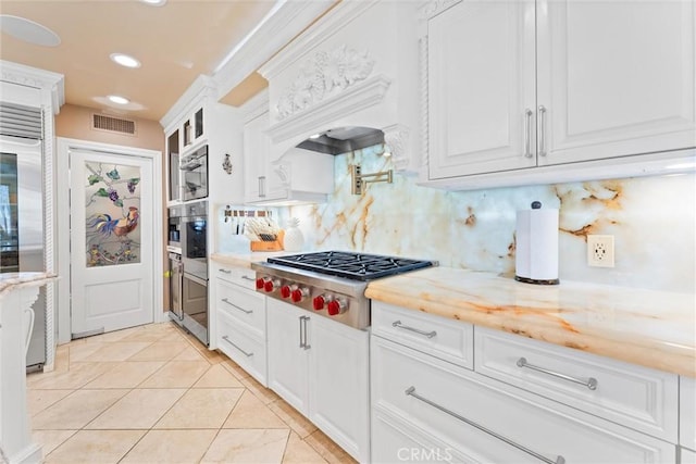 kitchen featuring decorative backsplash, appliances with stainless steel finishes, light stone countertops, white cabinets, and light tile patterned flooring