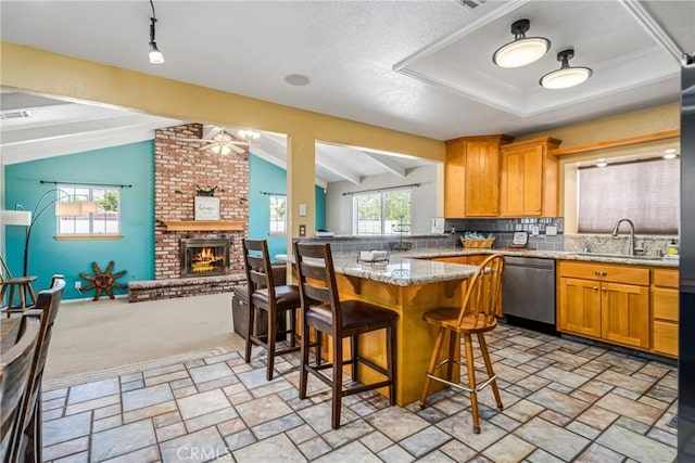 kitchen featuring a breakfast bar, lofted ceiling, stainless steel dishwasher, a fireplace, and light stone counters