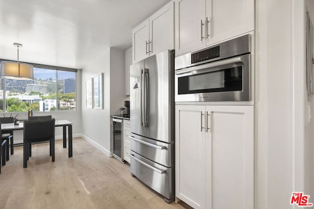 kitchen with appliances with stainless steel finishes, hanging light fixtures, light hardwood / wood-style floors, and white cabinets