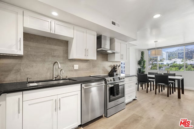 kitchen with appliances with stainless steel finishes, white cabinetry, wall chimney range hood, and light hardwood / wood-style flooring