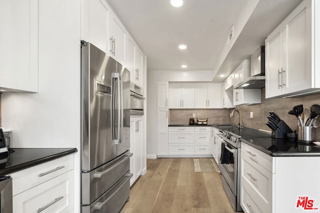 kitchen featuring light hardwood / wood-style floors, wall chimney range hood, stainless steel appliances, and white cabinets