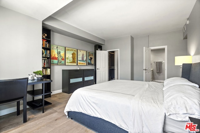 bedroom featuring ensuite bath, hardwood / wood-style floors, and a walk in closet