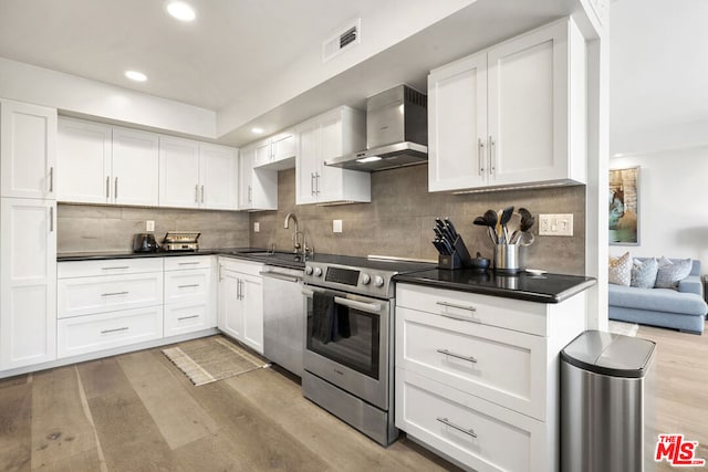 kitchen with white cabinets, sink, wall chimney exhaust hood, stainless steel appliances, and light hardwood / wood-style floors