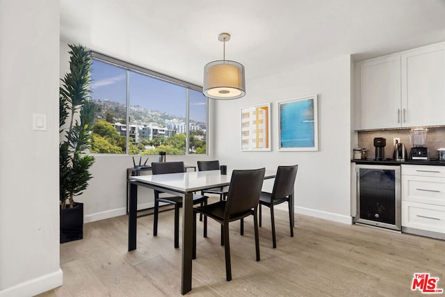 dining space featuring beverage cooler, light wood-type flooring, and bar