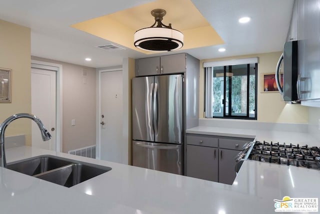 kitchen with appliances with stainless steel finishes, gray cabinetry, a raised ceiling, and sink