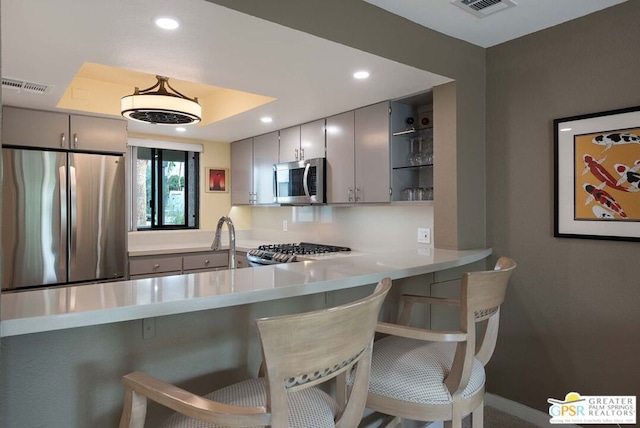 kitchen with kitchen peninsula, gray cabinetry, stainless steel appliances, and a kitchen bar