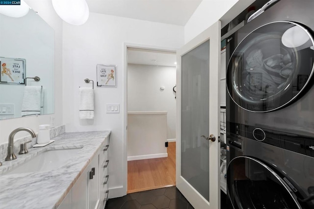 laundry room featuring dark tile patterned flooring, stacked washer and dryer, and sink