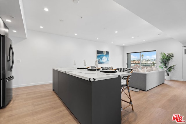 kitchen featuring a breakfast bar, light hardwood / wood-style flooring, light stone countertops, a spacious island, and stainless steel fridge