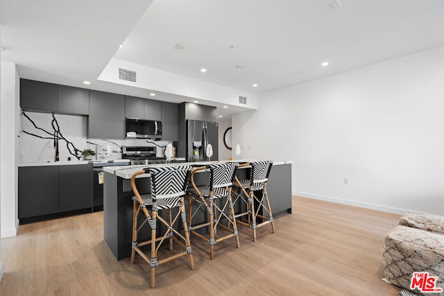 kitchen featuring a kitchen bar, stainless steel appliances, a center island, light hardwood / wood-style floors, and decorative backsplash