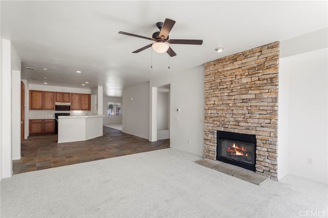 unfurnished living room featuring ceiling fan, dark carpet, and a stone fireplace