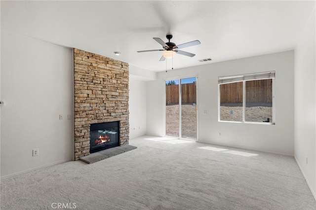 unfurnished living room with ceiling fan, light colored carpet, and a stone fireplace