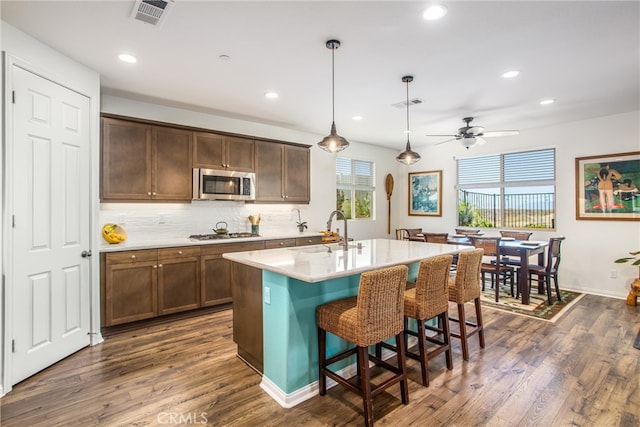 kitchen with a center island with sink, hanging light fixtures, dark hardwood / wood-style flooring, a kitchen breakfast bar, and stainless steel appliances