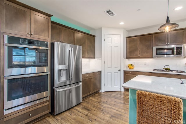 kitchen with decorative backsplash, hardwood / wood-style floors, pendant lighting, dark brown cabinetry, and stainless steel appliances