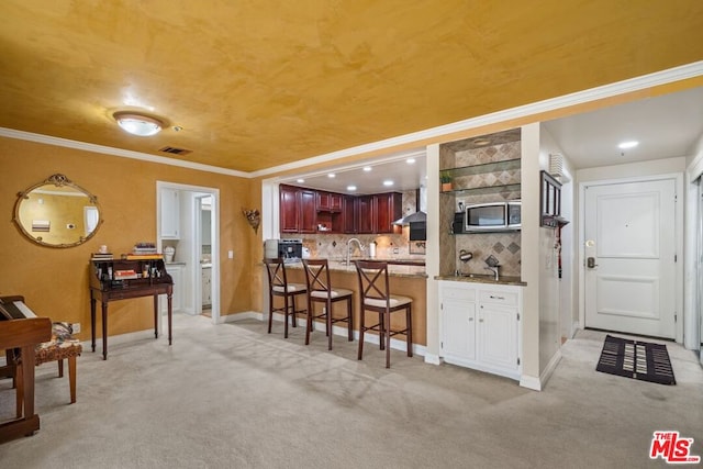 kitchen with decorative backsplash, kitchen peninsula, wall chimney exhaust hood, ornamental molding, and light colored carpet