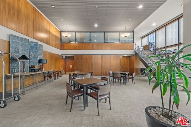 carpeted dining room with wooden walls and a high ceiling