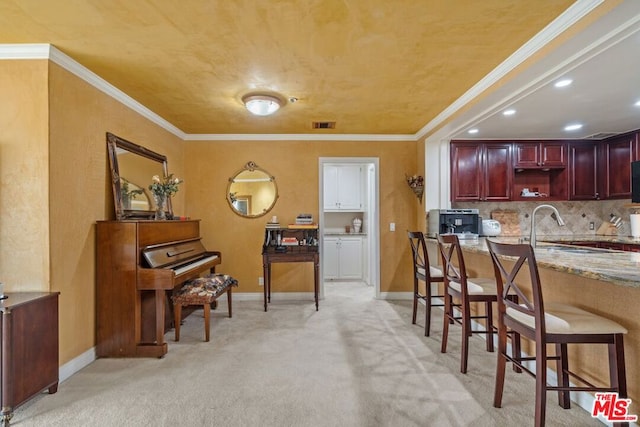 kitchen with a kitchen bar, ornamental molding, light carpet, and tasteful backsplash