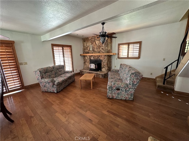 living room with ceiling fan, a stone fireplace, dark wood-type flooring, and a wealth of natural light