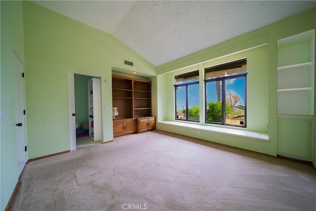 unfurnished bedroom with a textured ceiling, vaulted ceiling, and light colored carpet