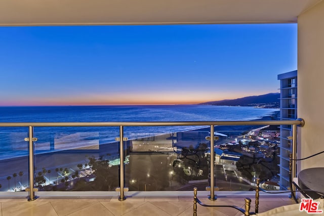 balcony at dusk featuring a water view