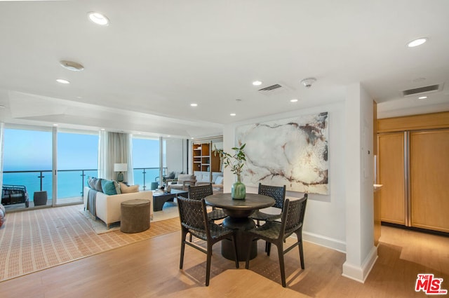 dining area with a water view, floor to ceiling windows, and light hardwood / wood-style flooring