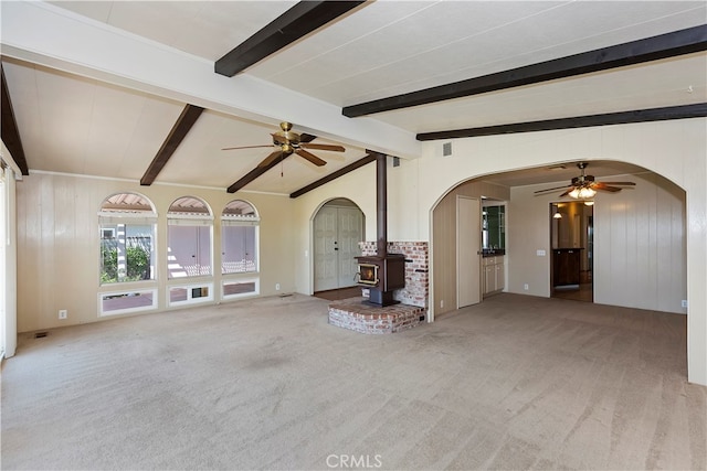 unfurnished living room featuring ceiling fan, light colored carpet, vaulted ceiling with beams, and a wood stove