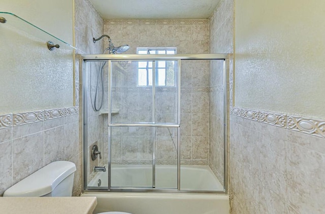 full bathroom featuring vanity, toilet, combined bath / shower with glass door, and tile walls