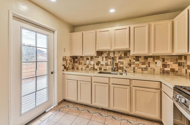 kitchen with backsplash, sink, light tile patterned floors, stainless steel range oven, and white cabinets