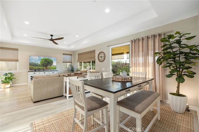 dining room with light wood finished floors, baseboards, a tray ceiling, and recessed lighting