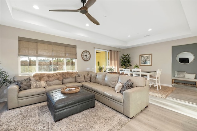 living room with light wood-type flooring, a raised ceiling, and ceiling fan