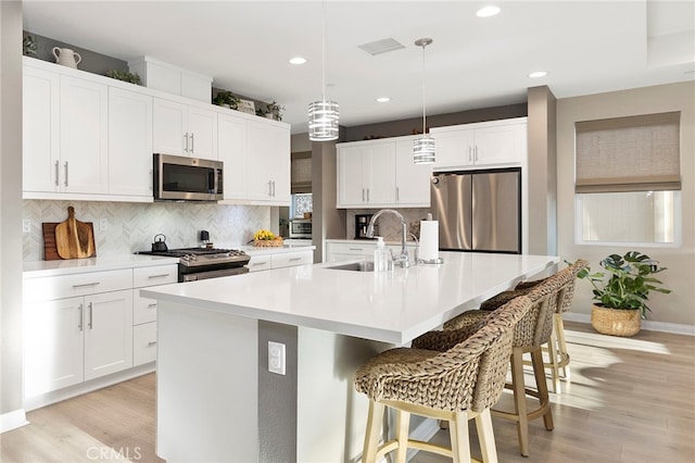 kitchen featuring light hardwood / wood-style floors, an island with sink, white cabinets, stainless steel appliances, and sink