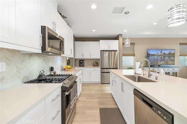 kitchen featuring stainless steel appliances, light countertops, pendant lighting, a sink, and recessed lighting