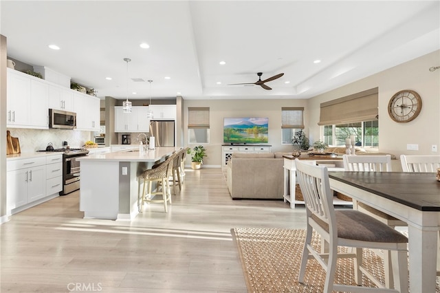 dining space with ceiling fan, sink, light hardwood / wood-style flooring, and a raised ceiling