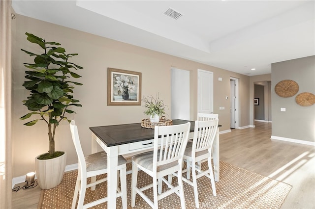 dining room featuring a tray ceiling, light wood finished floors, visible vents, and baseboards