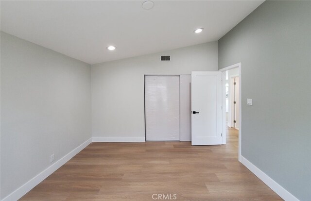 unfurnished bedroom with vaulted ceiling, a closet, and light hardwood / wood-style flooring