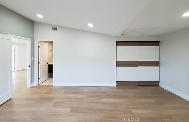 unfurnished bedroom with ensuite bathroom, a closet, light hardwood / wood-style floors, and lofted ceiling