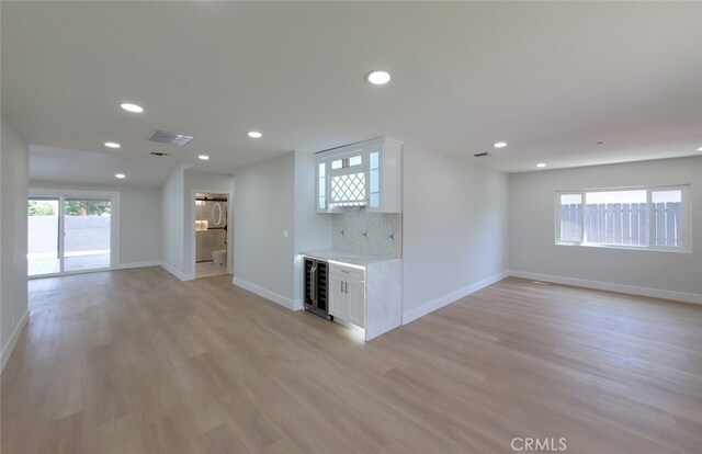 unfurnished living room featuring light wood-type flooring, a wealth of natural light, and indoor bar