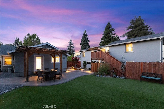 back house at dusk featuring a lawn and a patio