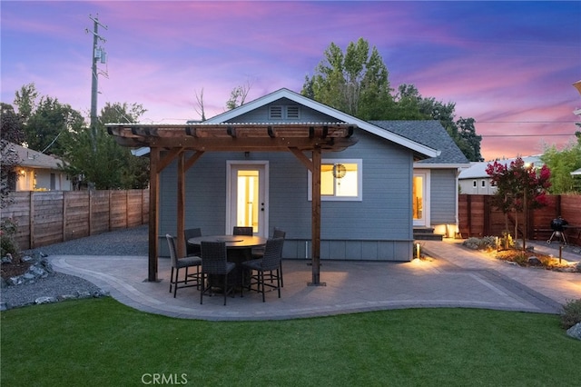 back house at dusk featuring a lawn, a patio, and a pergola