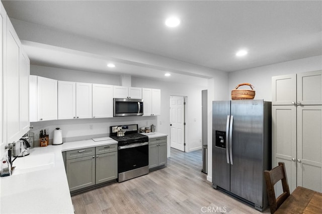 kitchen featuring gray cabinets, sink, white cabinets, light hardwood / wood-style flooring, and stainless steel appliances