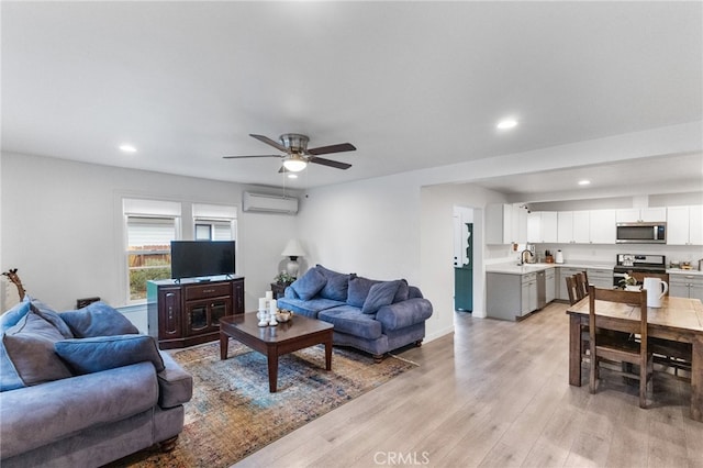 living room with ceiling fan, light hardwood / wood-style flooring, sink, and a wall unit AC