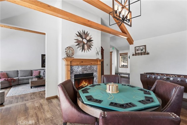 dining space featuring vaulted ceiling with beams, a premium fireplace, wood-type flooring, and an inviting chandelier