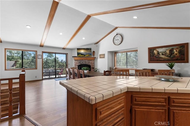 kitchen featuring tile countertops, light wood-type flooring, a fireplace, and vaulted ceiling