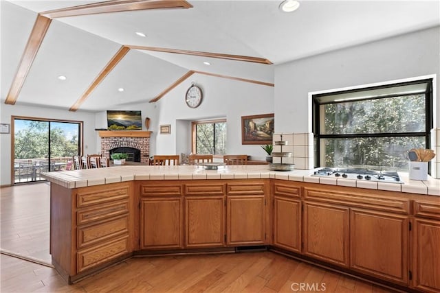 kitchen featuring tile countertops, a brick fireplace, a healthy amount of sunlight, and stainless steel gas stovetop