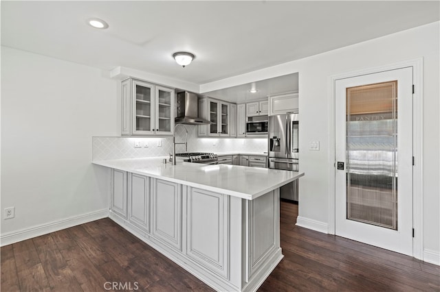 kitchen with appliances with stainless steel finishes, dark wood-type flooring, tasteful backsplash, kitchen peninsula, and wall chimney range hood